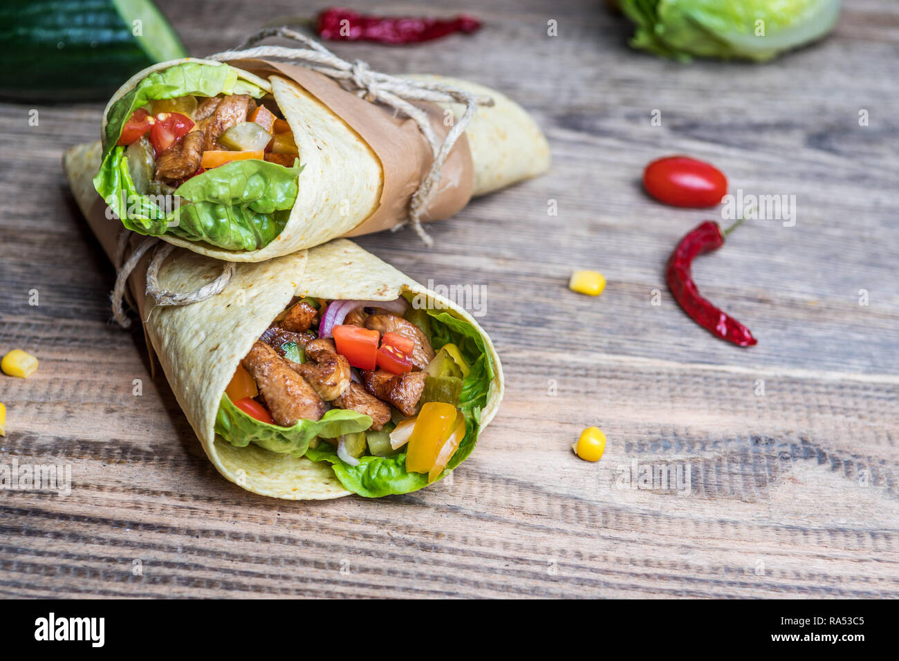 Traditional mexican tortilla wrap with vegetables and grilled chicken meat on wood table Stock Photo