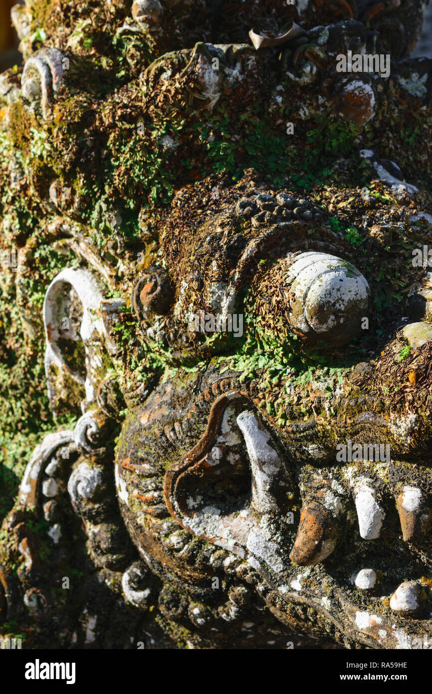 Very old dragon head shape stone sculpture covered with moss and lichens in Bali Stock Photo