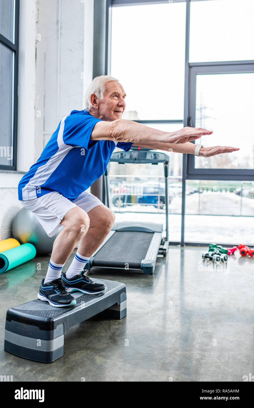 side view of senior sportsman doing squats on step platform at gym