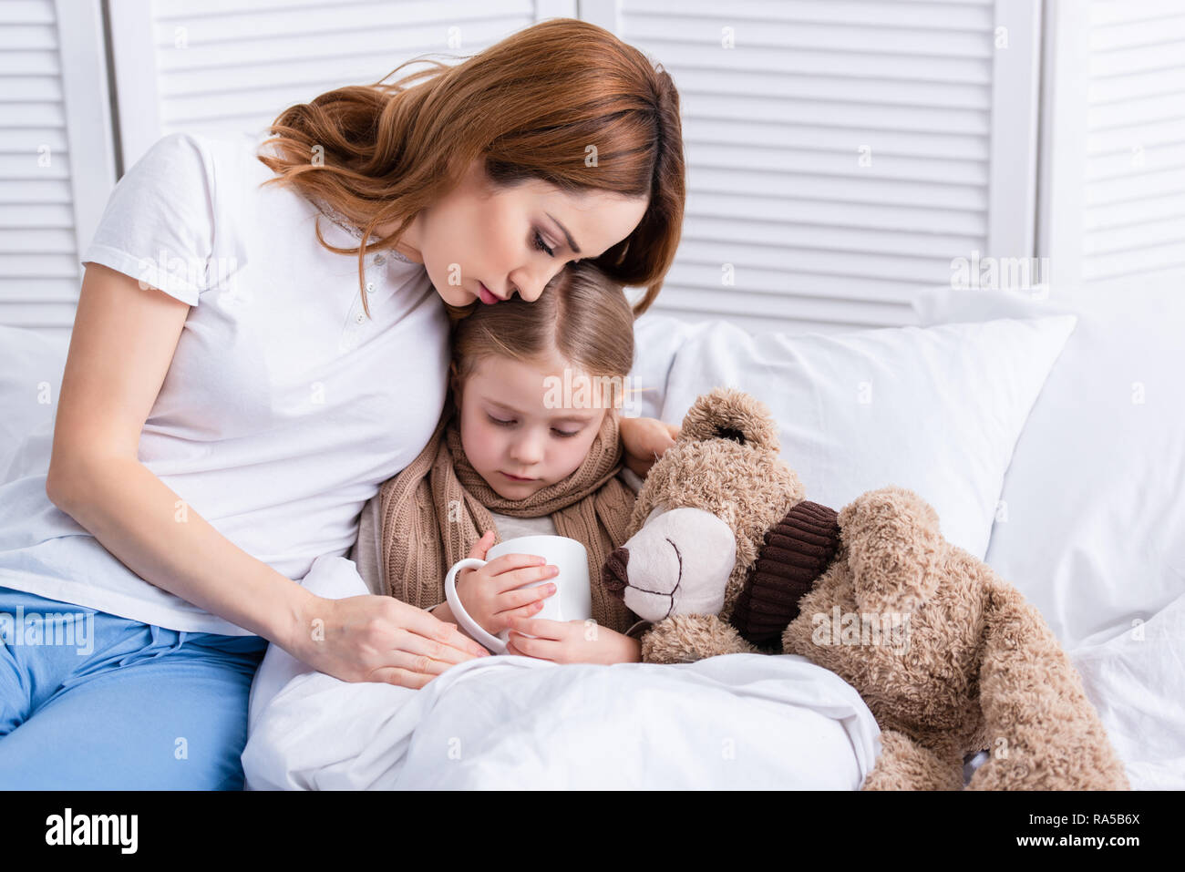 mother taking care of sick daughter and hugging her in bedroom Stock ...