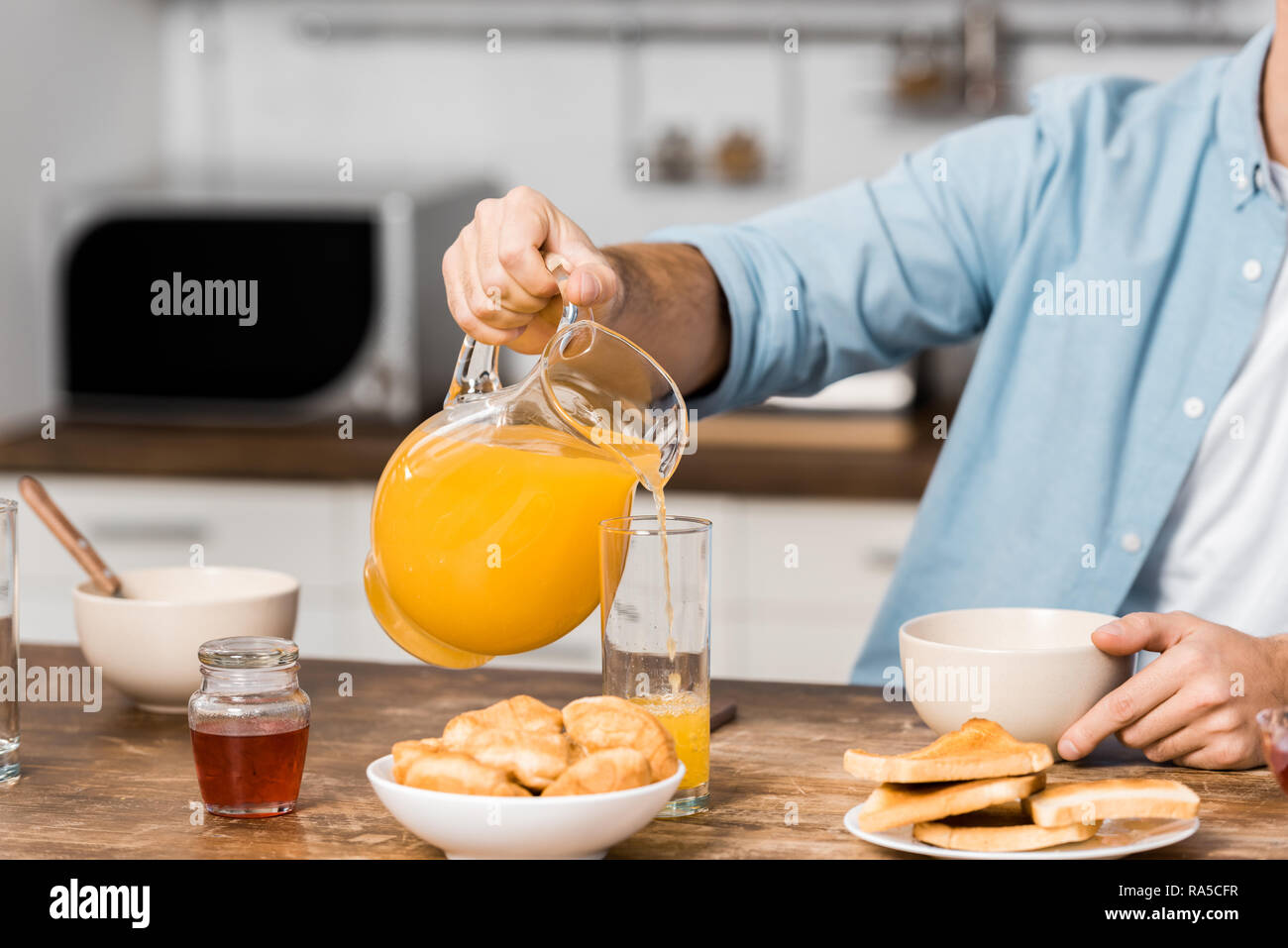 cropped view of man pouring orange juice in glass on kitchen table Stock Photo