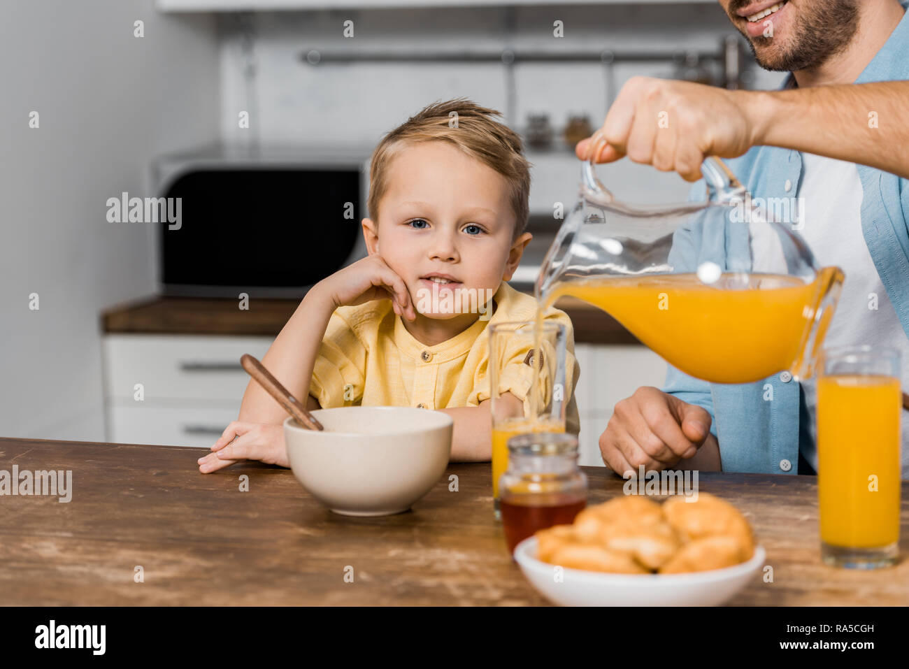 cropped view of smiling father pouring orange juice in glass and cute boy looking at camera Stock Photo