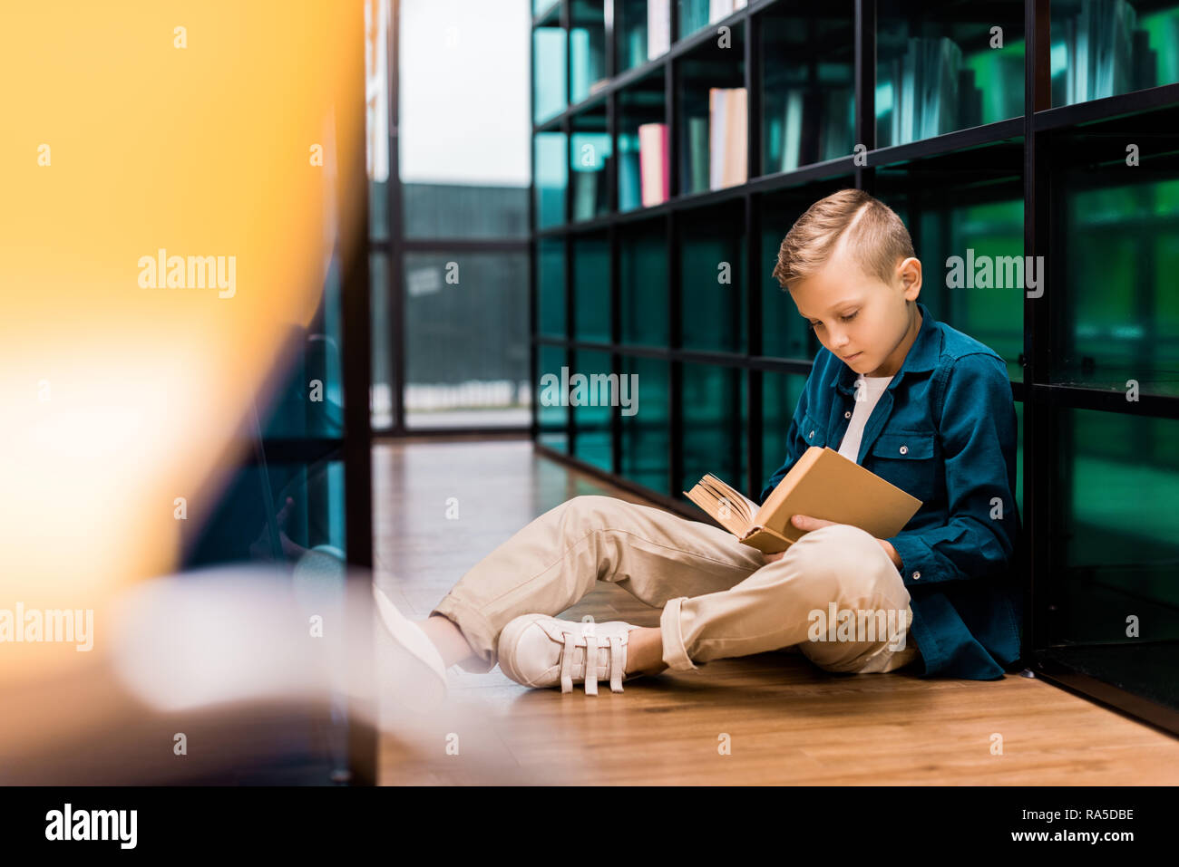 cute focused boy reading book and sitting on floor in library Stock ...