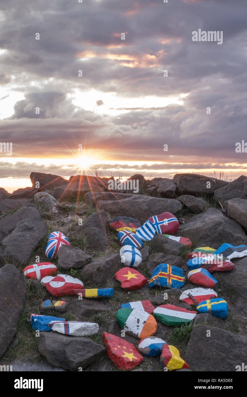 Different national flags painted on stones outdoors in Borgarfjordur in Iceland during beautiful sunset. Travel and national concept. Stock Photo