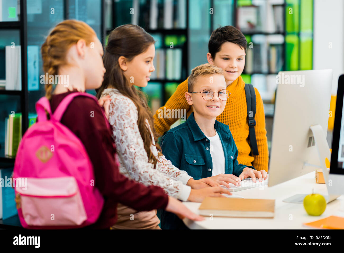 boy smiling at camera while using computer with classmates in library Stock Photo