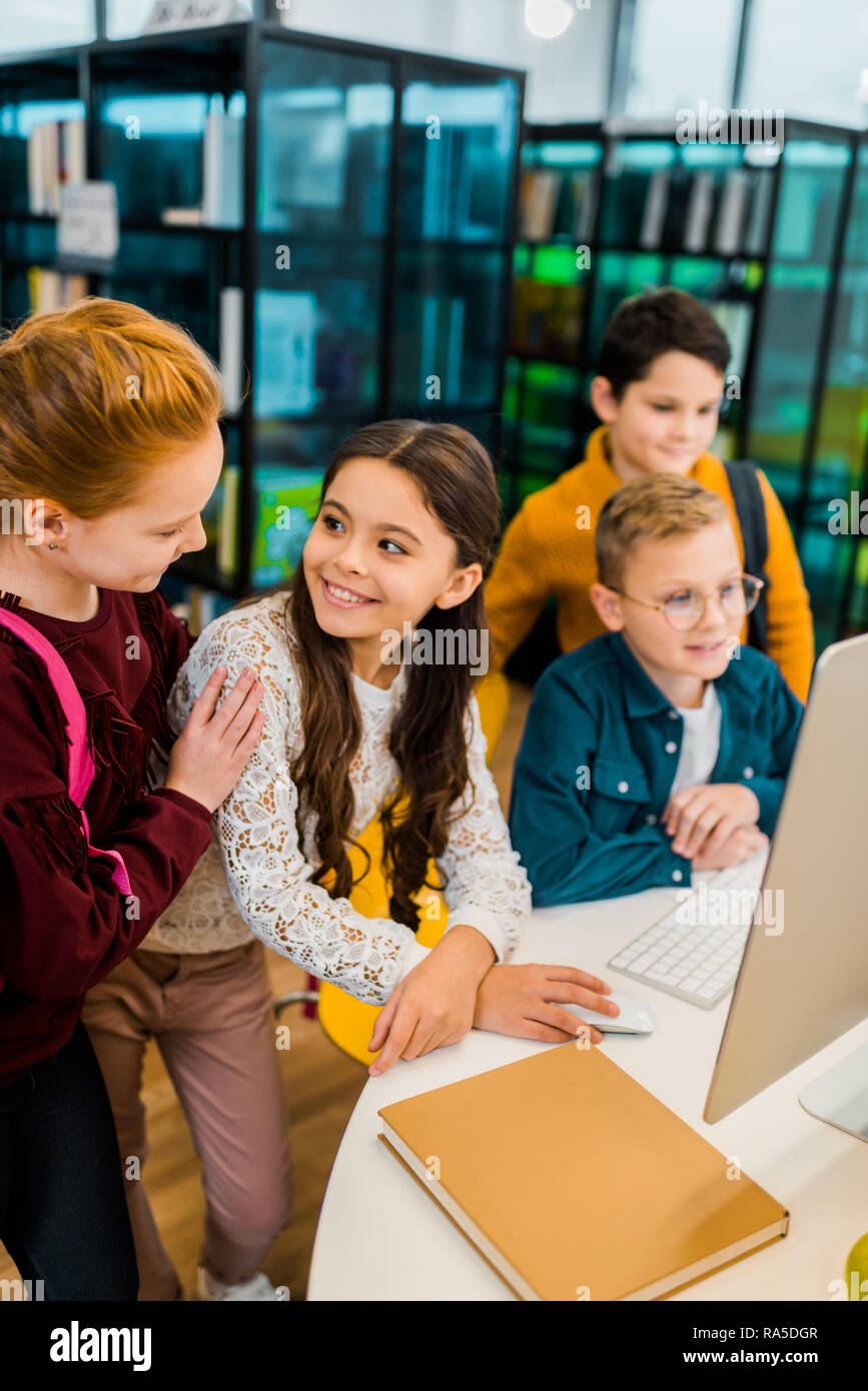 beautiful happy schoolchildren using desktop computer together in library Stock Photo