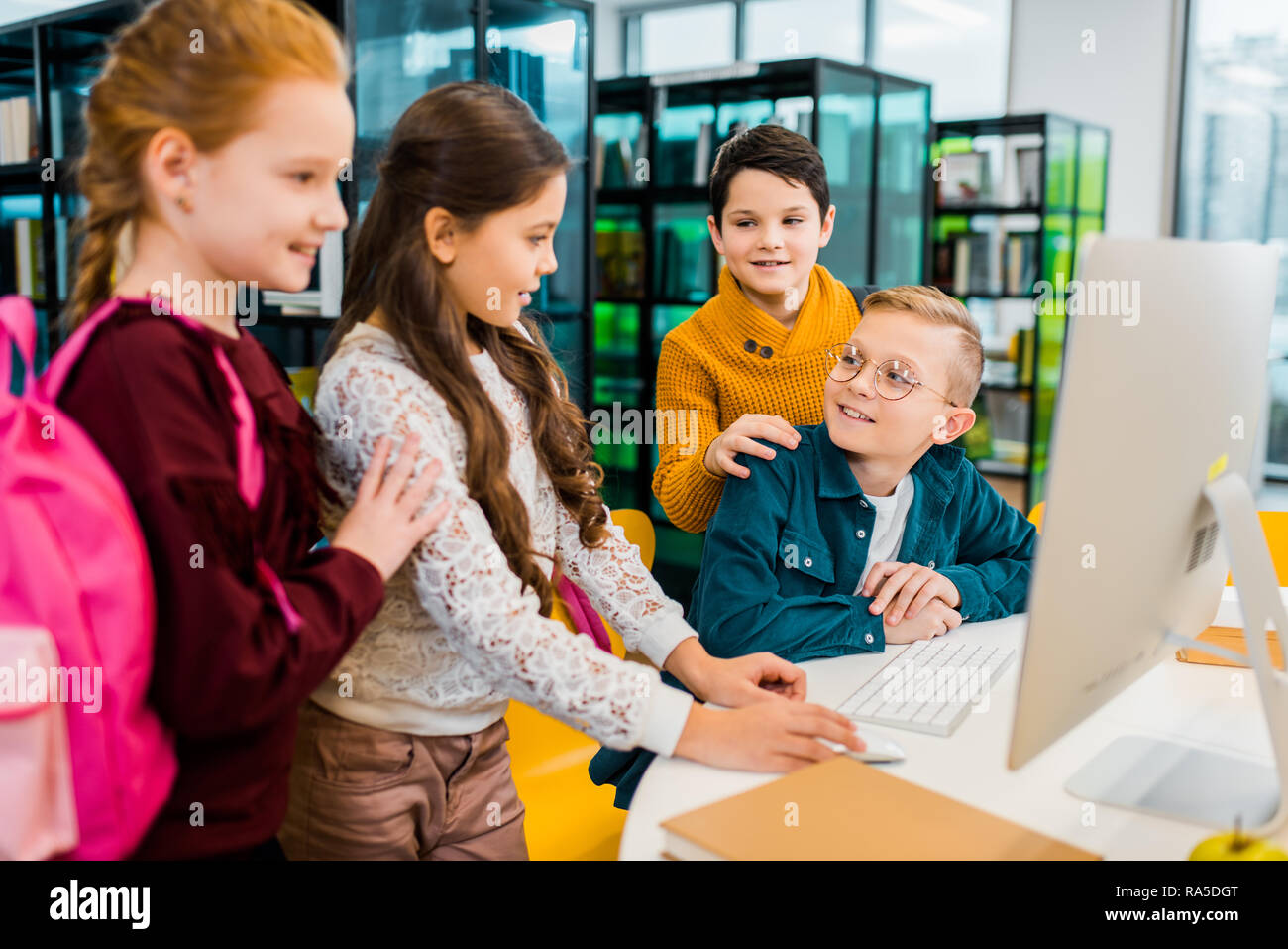 cute smiling schoolchildren using desktop computer together in library Stock Photo