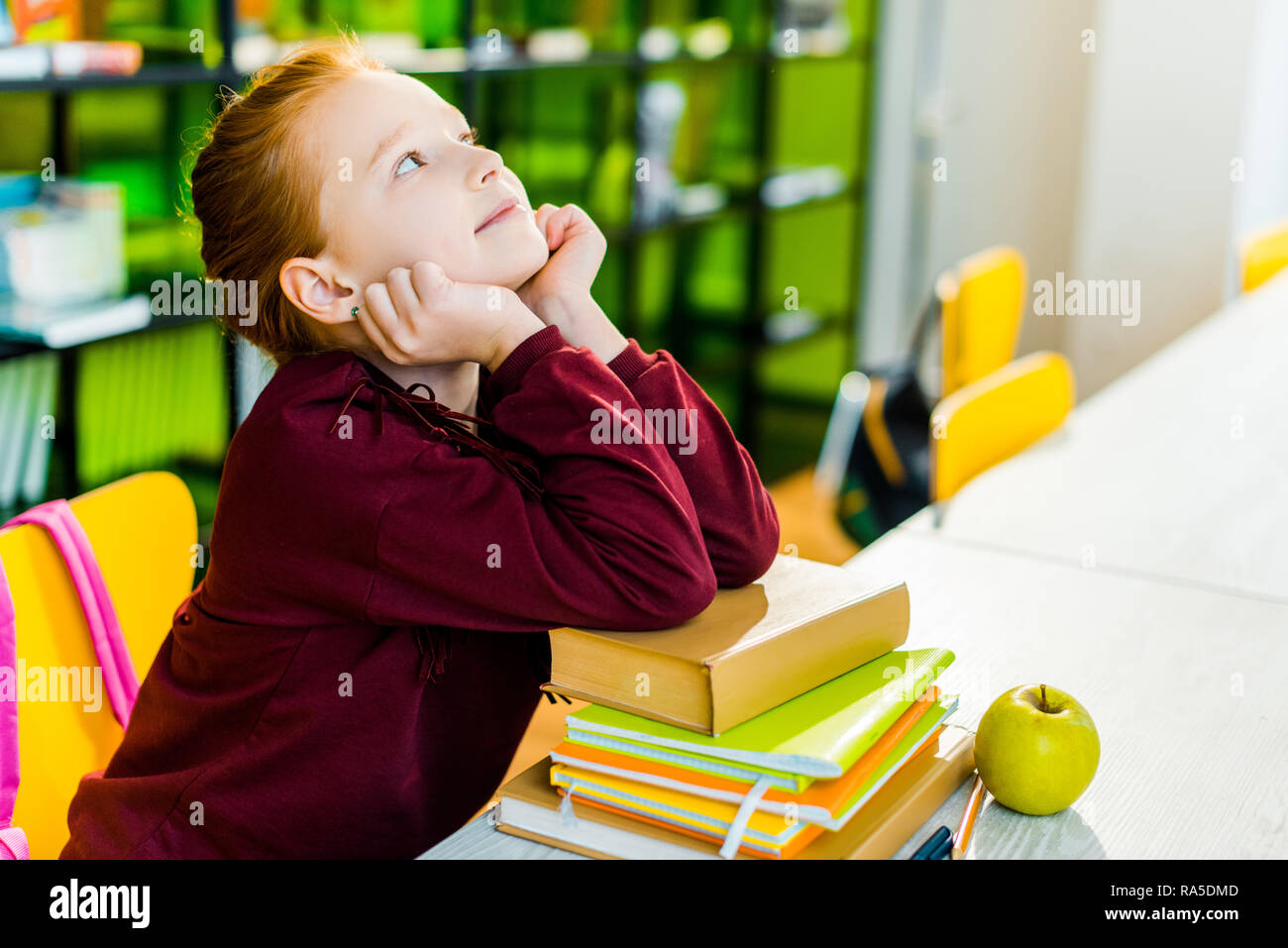 adorable schoolgirl sitting at desk with books and looking up in ...