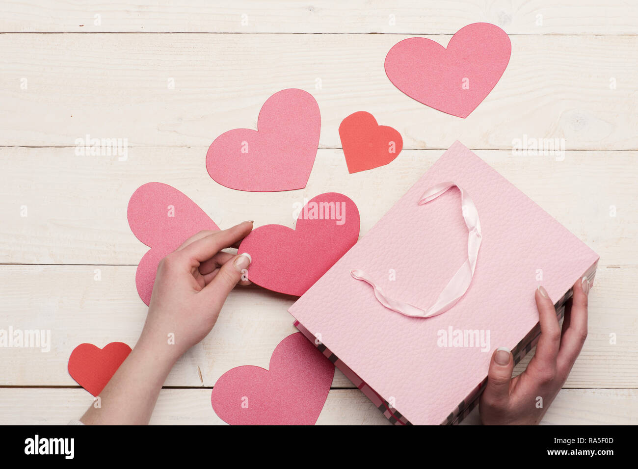 Love and holiday concept. Female hand holding pink heart. Pink paper bag with Valentines on vintage background. Valentines day cards or decorations, top view. Stock Photo