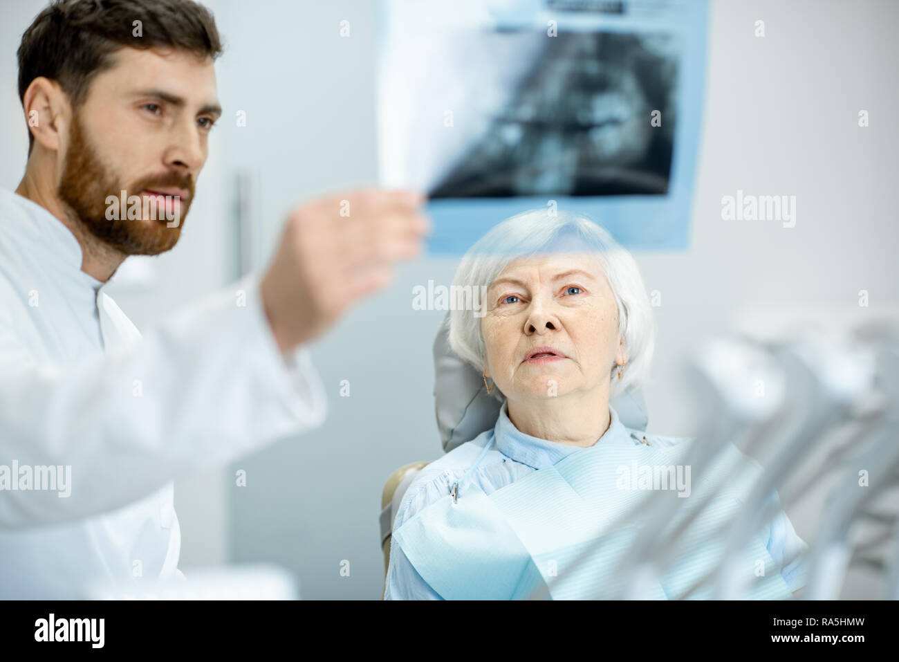 Worried elder woman during the consultation with handsome dentist showing panoramic x-ray in the dental office Stock Photo