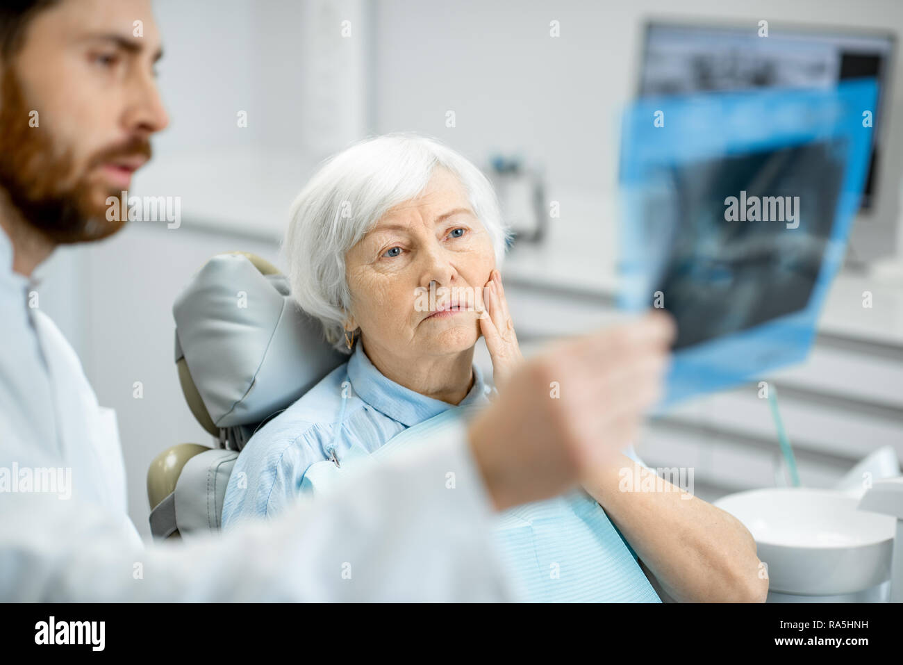 Worried elder woman during the consultation with handsome dentist showing panoramic x-ray in the dental office Stock Photo