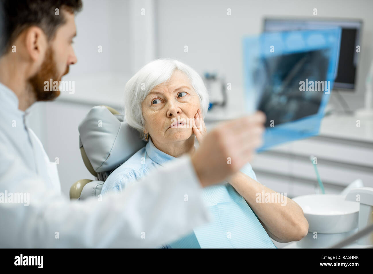 Worried elder woman during the consultation with handsome dentist showing panoramic x-ray in the dental office Stock Photo