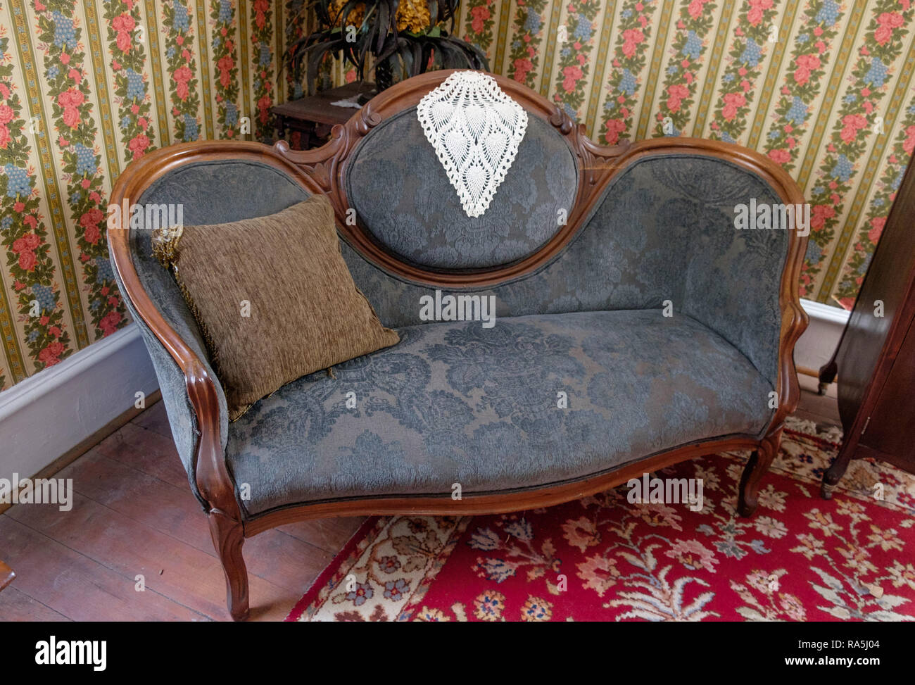 Antique couch with doily, throw pillow, pink & blue vintage floral wall paper & vintage rug. Interior of old home, Chestnut Square, McKinney Texas. Stock Photo