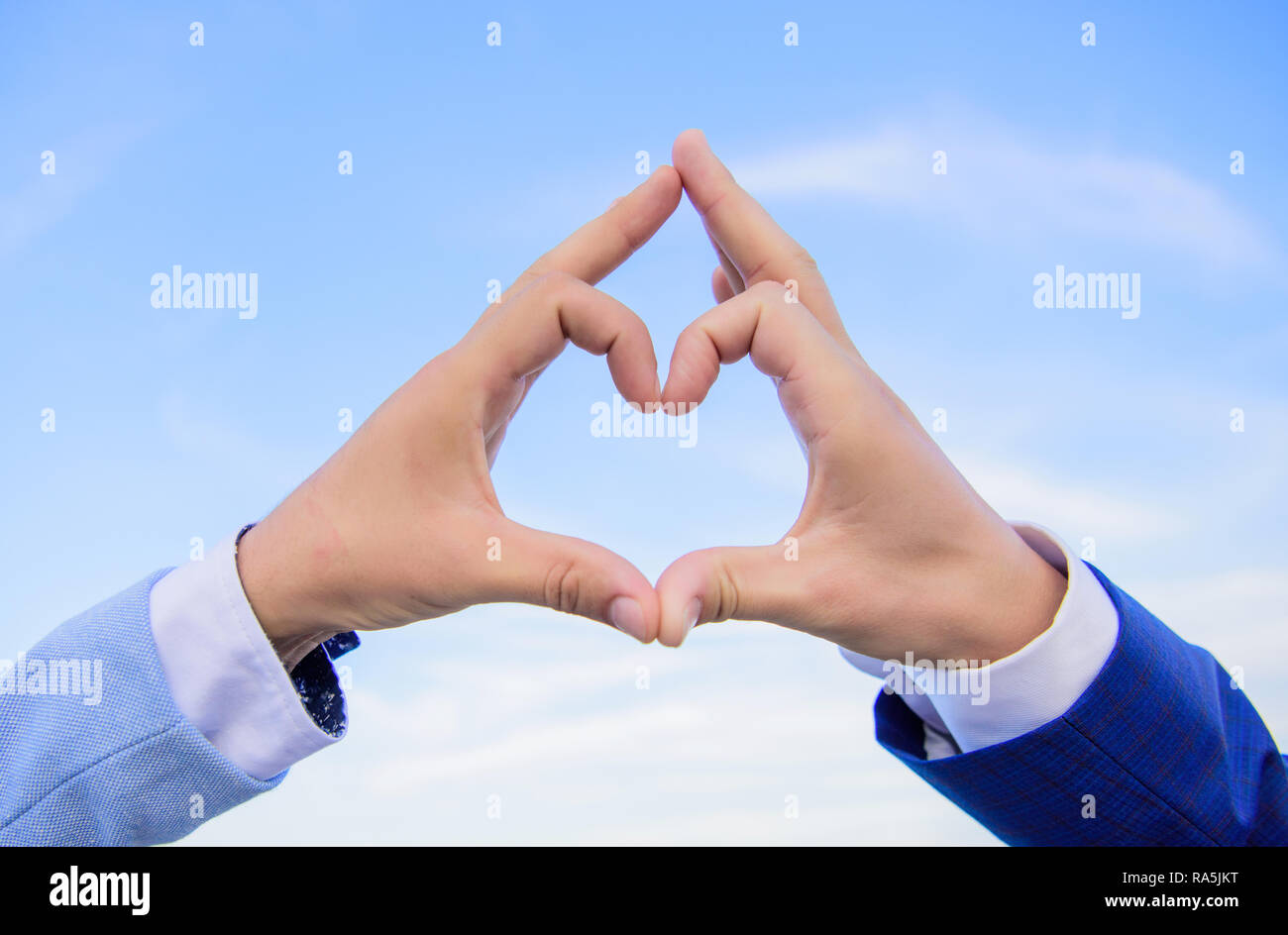 Hands put together in heart shape blue sky background. Love symbol concept.  Male hands in heart shape gesture symbol of love and romance. Hand heart  gesture forms shape using fingers Stock Photo -