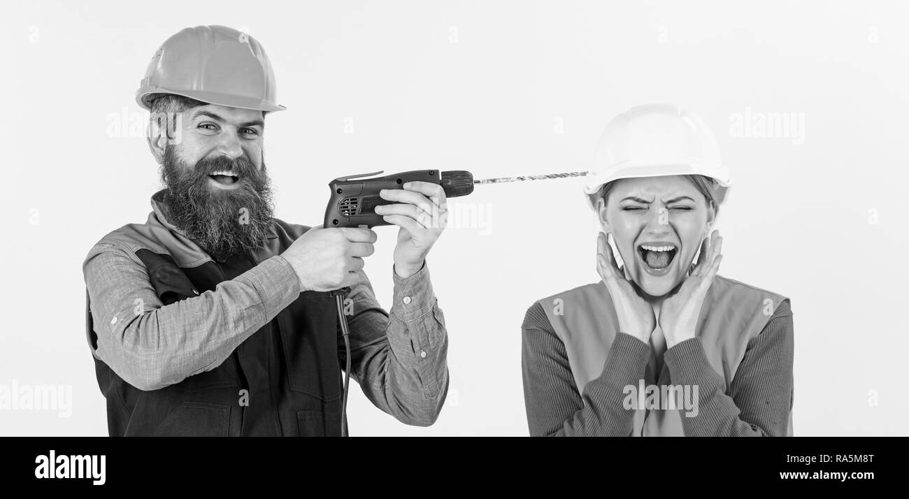 Builder, repairman makes hole in female head. Woman on scared face in helmet, hard hat. Husband annoying his wife. Annoying repair concept. Man with happy face drills head of woman, white background. Stock Photo