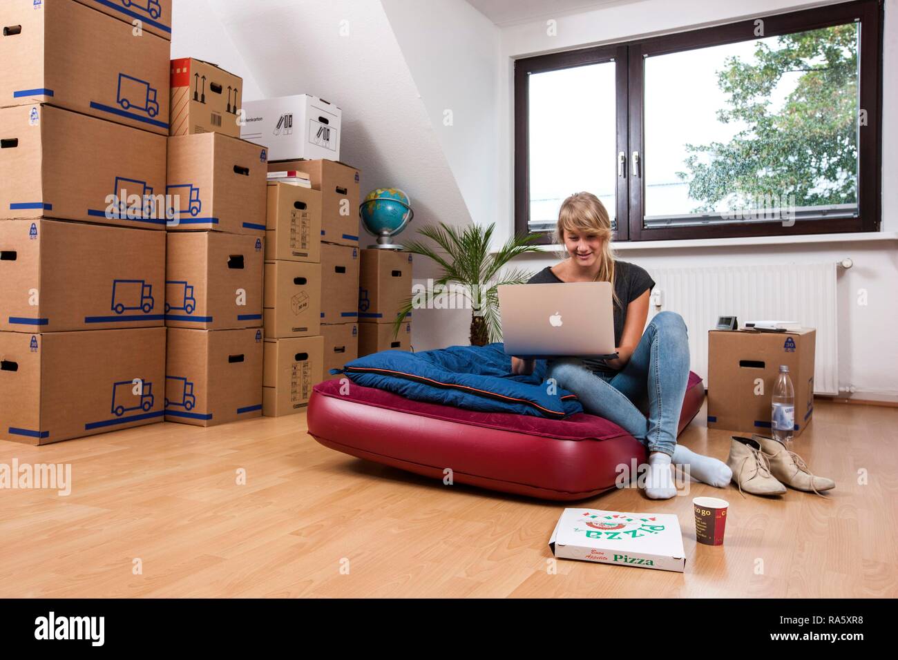 Young woman sitting in an empty room in a new apartment, provisionally furnished with a sleeping bag, an air mattress Stock Photo