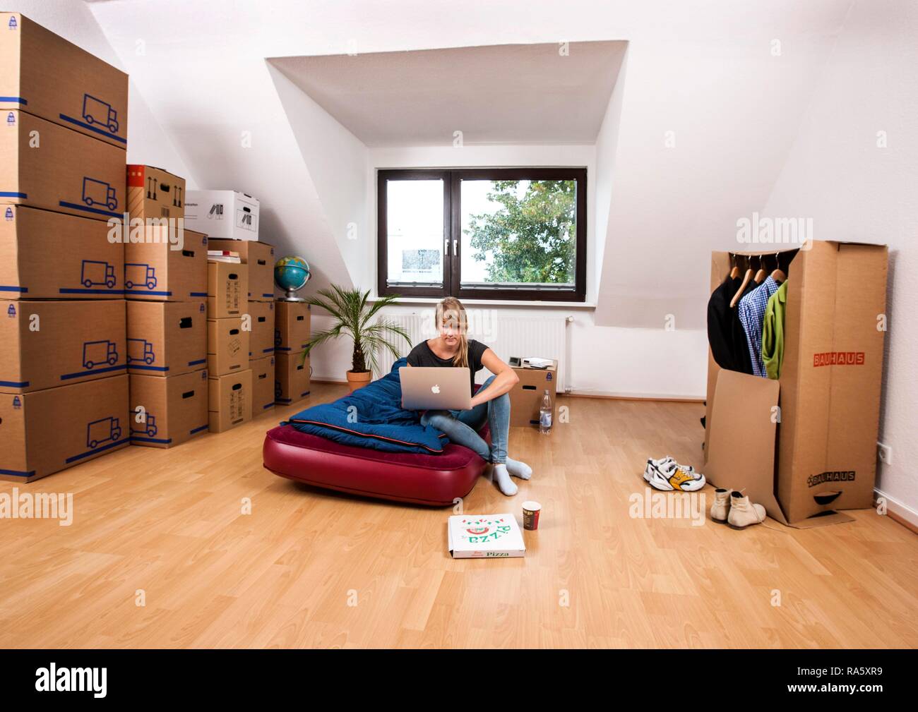 Young woman sitting in an empty room in a new apartment, provisionally furnished with a sleeping bag, an air mattress Stock Photo