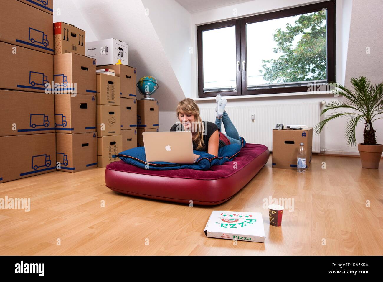 Young woman lying in an empty room in a new apartment, provisionally furnished with a sleeping bag, an air mattress Stock Photo