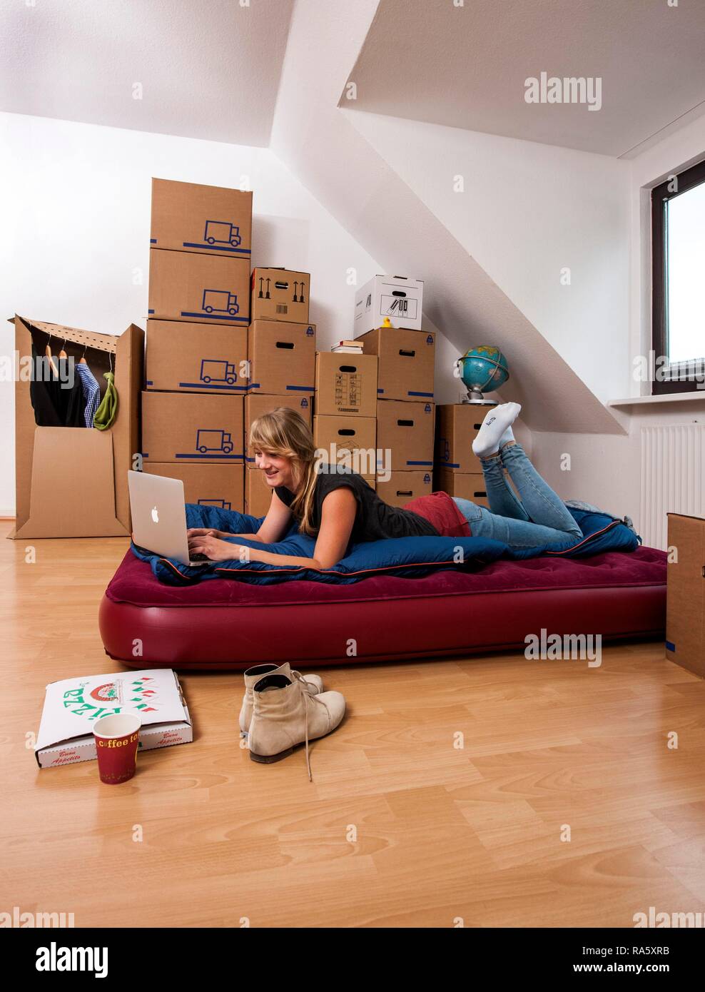 Young woman lying in an empty room in a new apartment, provisionally furnished with a sleeping bag, an air mattress Stock Photo