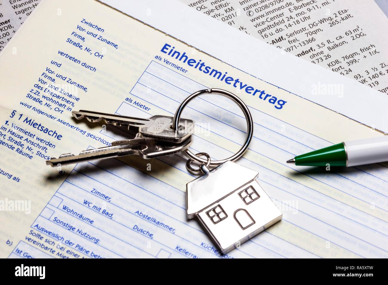 Two keys with a metal key tag shaped like a house lying on a German rental agreement, symbolic image for home, real estate Stock Photo