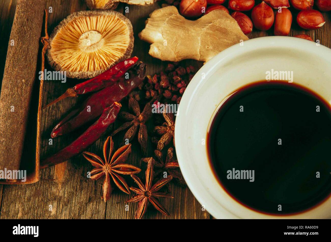 Lay flat of Chinese cooking spices including ginger, star anise, soy sauce, cinnamon bark, dry chili peppers, peanuts and others on wooden background Stock Photo