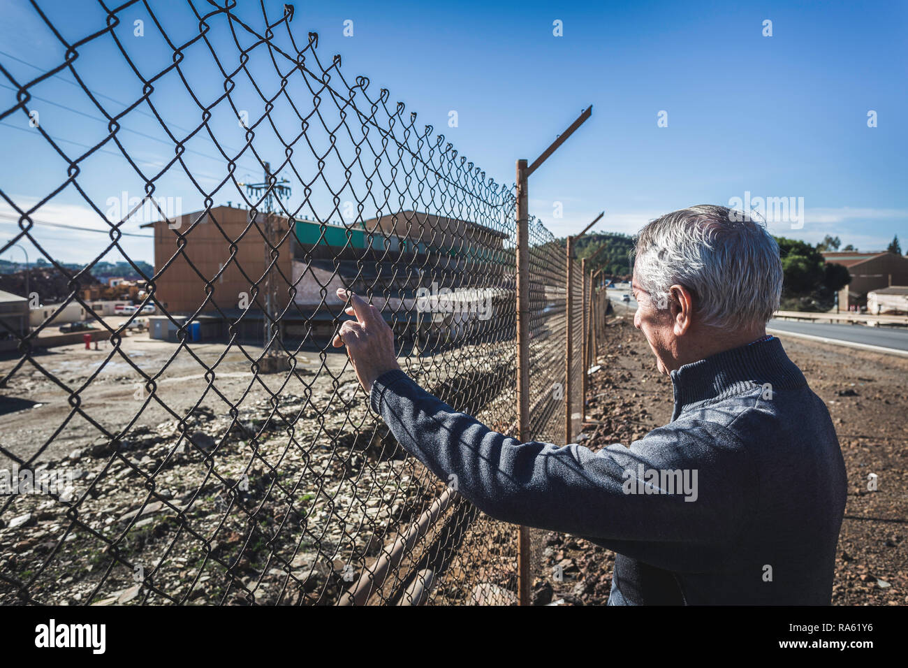 Elderly man looking through fence with blue sky background Stock Photo