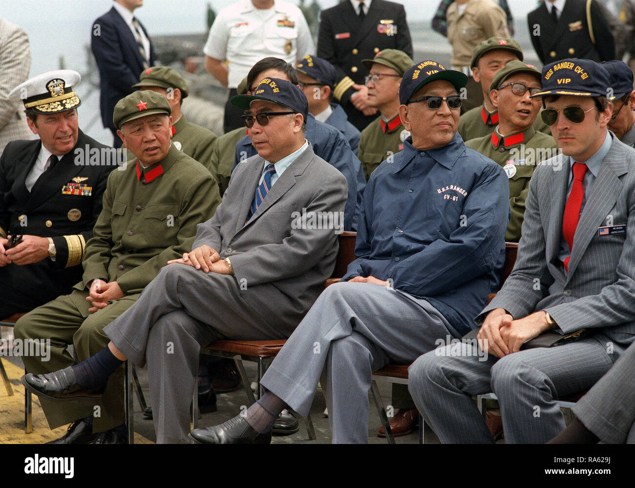 1980 - Vice Premier Geng Biao of China, in the blue jacket, and the Chinese ambassador sit with U.S. Navy officials aboard the aircraft carrier USS RANGER (CV-61).  They are waiting for the start of the air and sea demonstration. Stock Photo