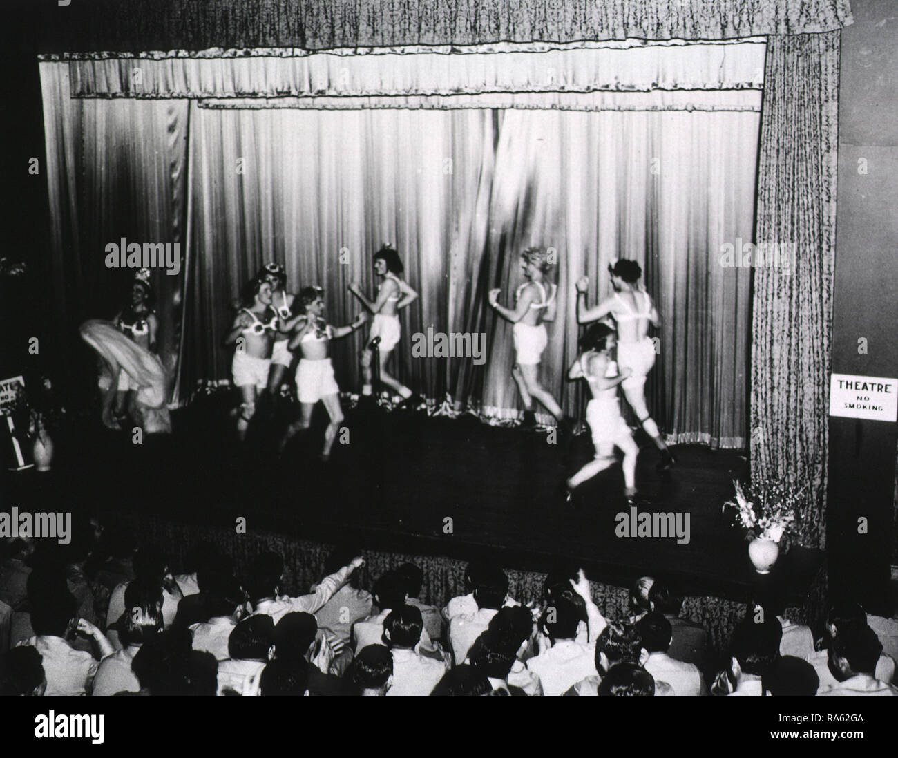 A group of men wearing wigs, bras, and bloomers dances across a stage in a  theater in front of an audience of servicemen Stock Photo - Alamy