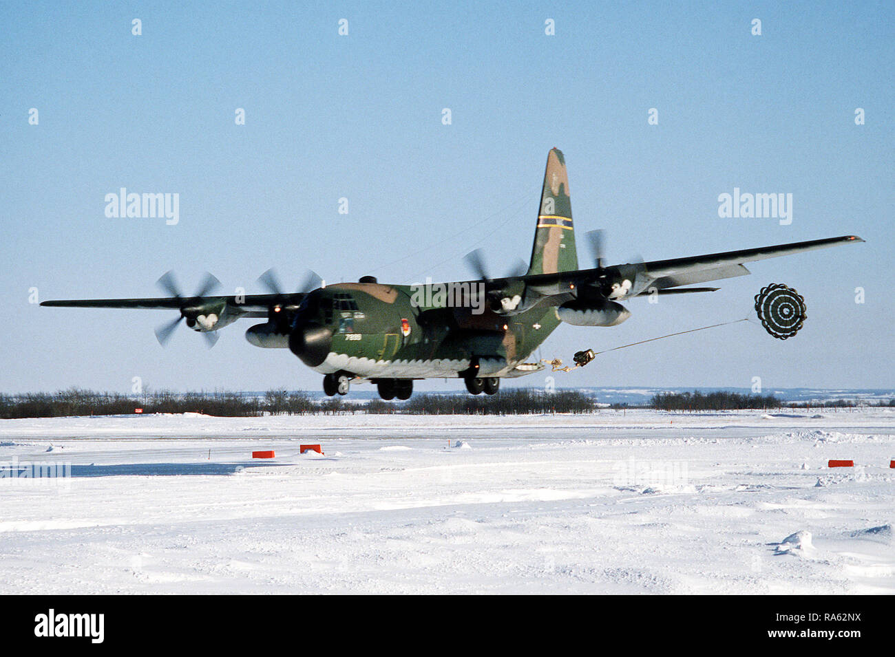 1979 - A U.S. Air Force C-130 Hercules aircraft makes a low-altitude parachute extraction system (LAPES) drop on a snow-covered runway during a test at Namo, Canadian Air Force Base. Stock Photo