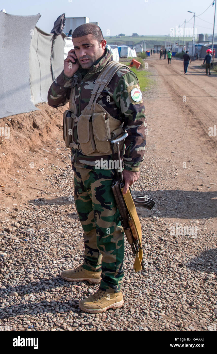 19 December 2018, Iraq, Hasan Sham: An armed employee of the domestic secret service of the Autonomous Region of Kurdistan, Asayî· (Asayesch) stands in the internally displaced person camp Hasan Sham and makes a phone call. The secret service was founded in September 1993 and is mainly used in the fight against terrorism. Hasan Sham's tent camp near the largely destroyed former IS stronghold of Mossul accommodates 3,300 of the 1.8 million internally displaced persons in Iraq. Photo: Jens Büttner/dpa-Zentralbild/ZB Stock Photo