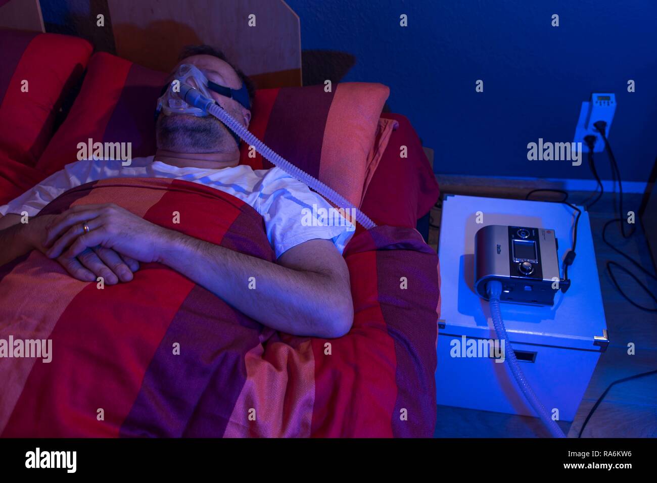 Man with sleep apnea syndrome, wears a CPAP mask while sleeping, breathing mask, which pushes air into the respiratory tract due Stock Photo