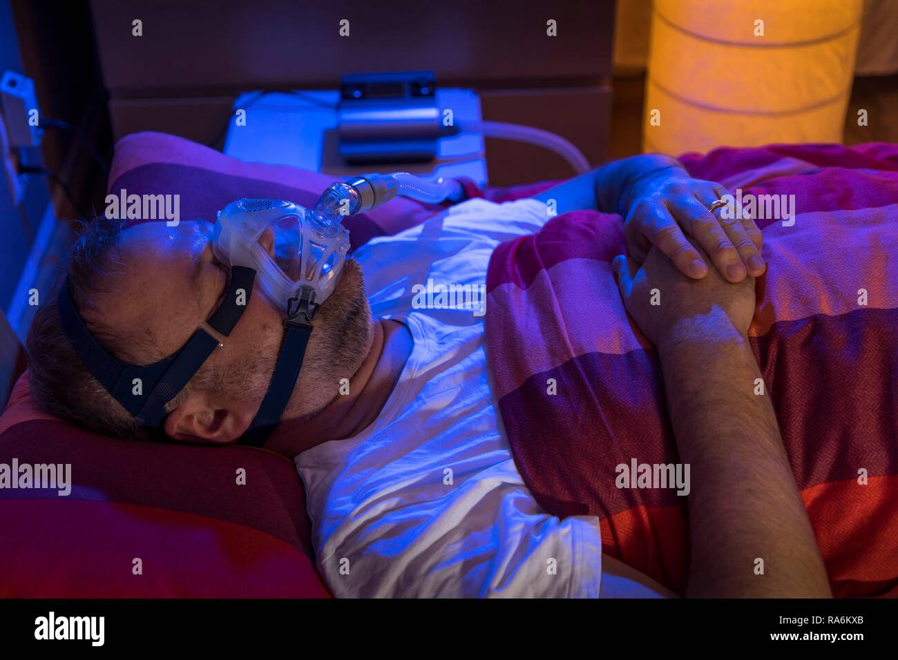 Man with sleep apnea syndrome, wears a CPAP mask while sleeping, breathing mask, which pushes air into the respiratory tract due Stock Photo