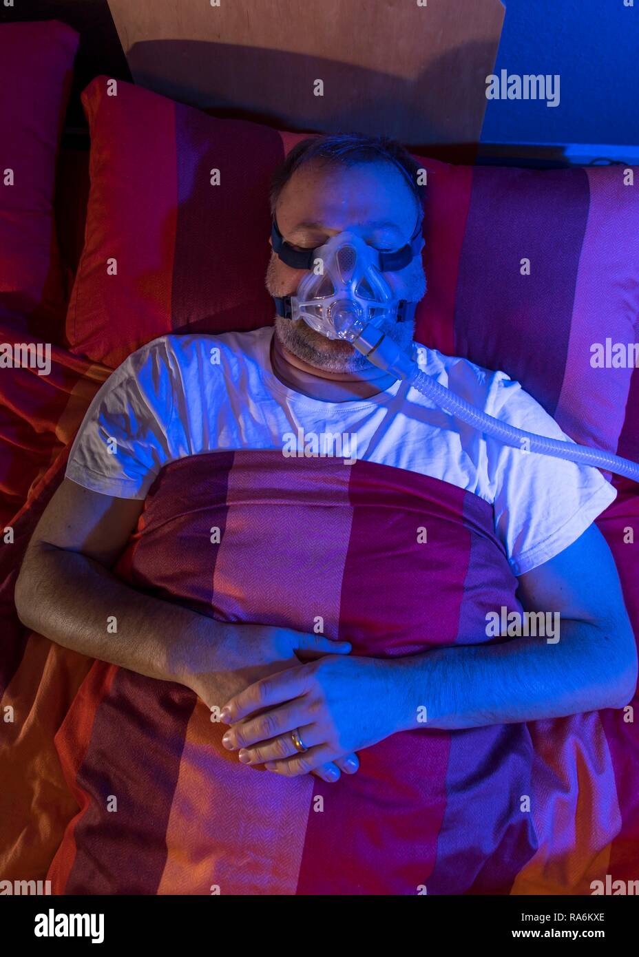 Man with sleep apnea syndrome, wears a CPAP mask while sleeping, breathing mask, which pushes air into the respiratory tract due Stock Photo