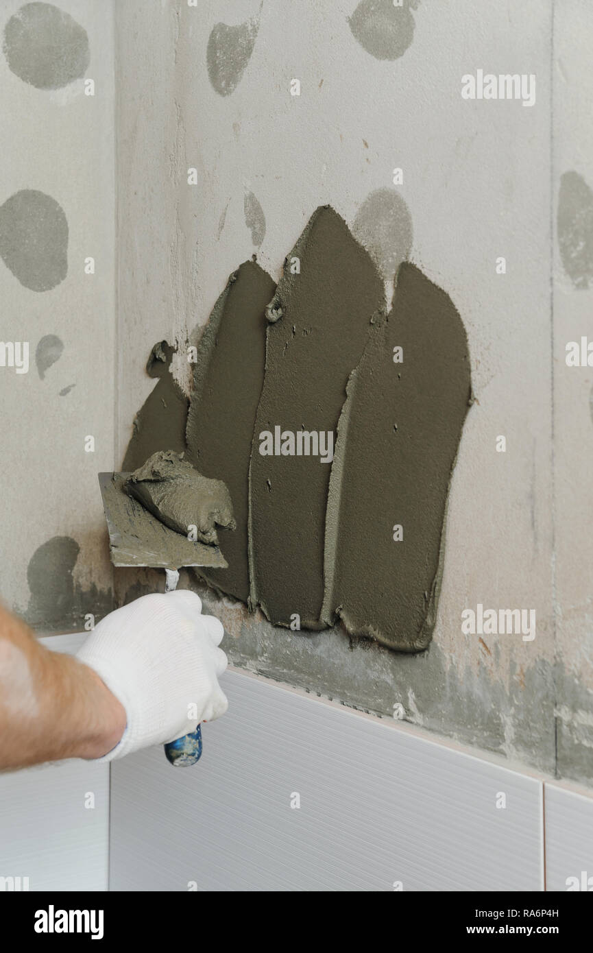 Installing the tiles on the wall. A worker putting adhesive on the wall