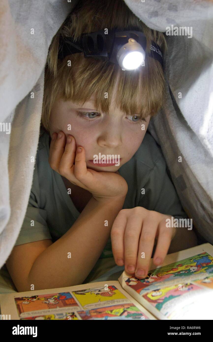 Boy reading a comic with a head lamp under the duvet Stock Photo