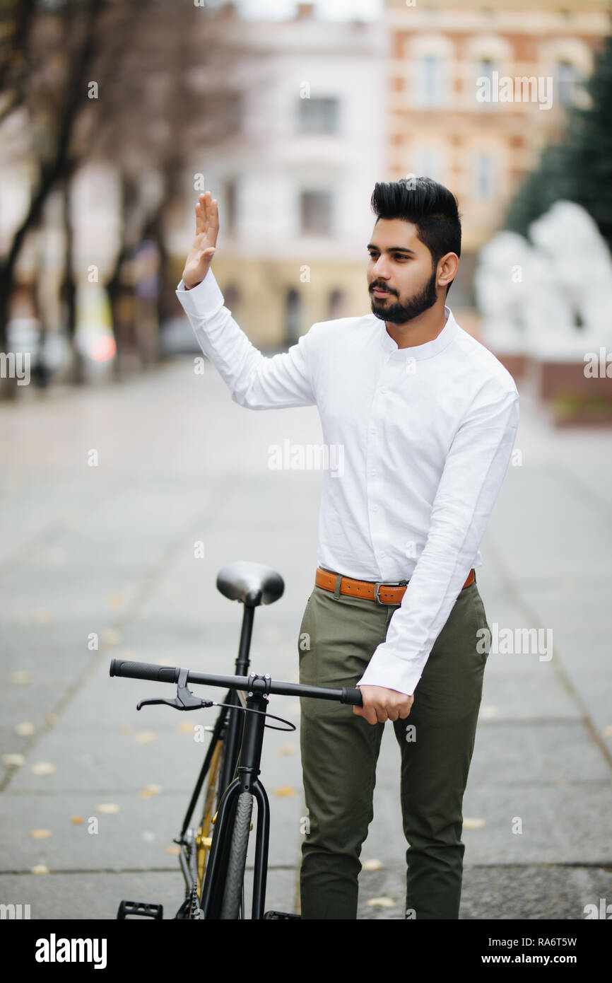 Young hipster man with fixed gear bike waving hand on city street Stock