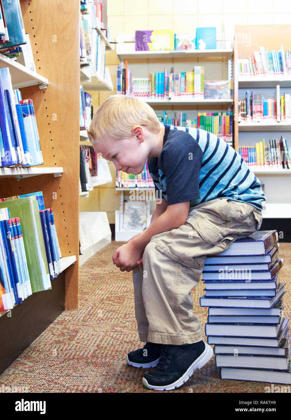 Young child sitting on a stack of books searching for the perfect book