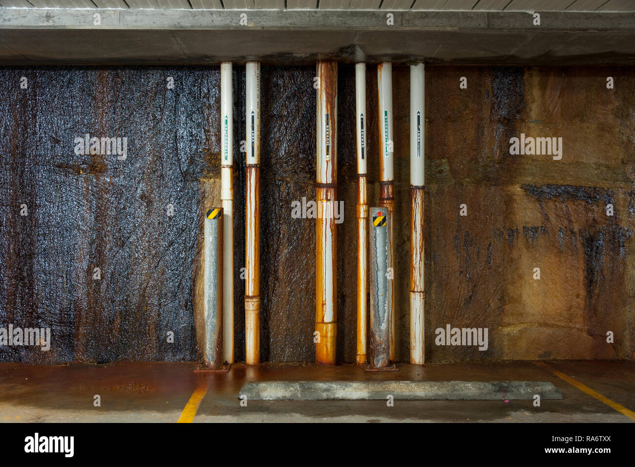Pipes running down a concrete wall with rust and corrosion problems Stock Photo