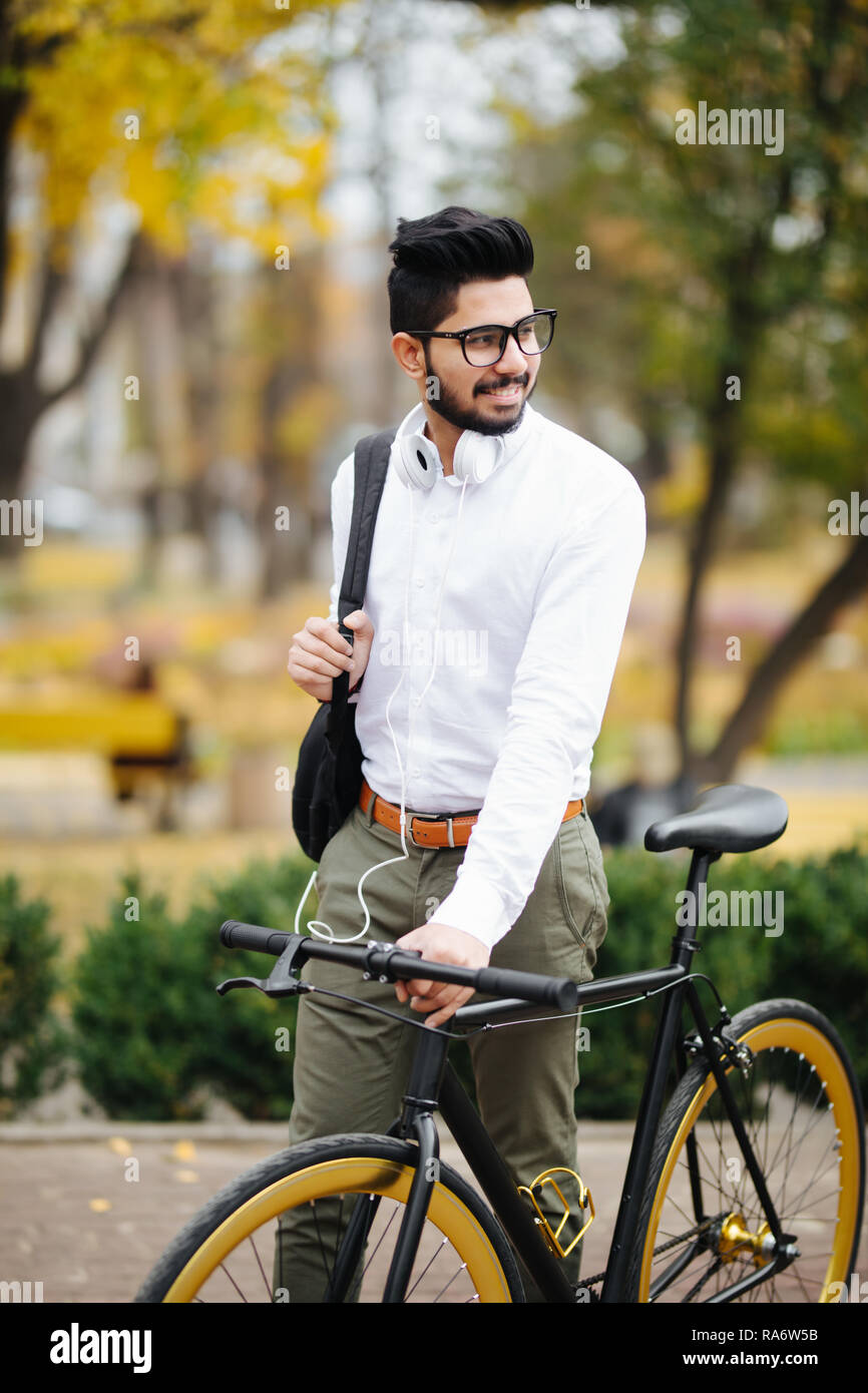 Indian bearded student man with backpack with bicycle walking on street Stock Photo