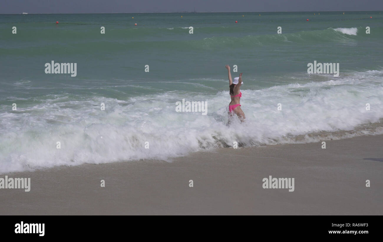 Teenage girl in a bathing suit happily jumps in waves of Persian Gulf on beach of Dubai Stock Photo