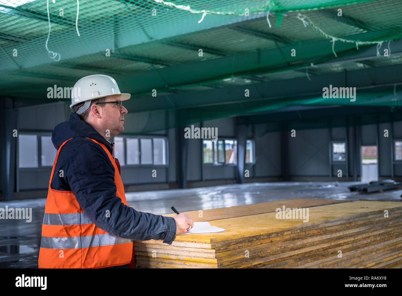 Portrait of development supervisor wearing protective vest and helmet proofing blueprints using a digital tablet inside unfinished building Stock Photo