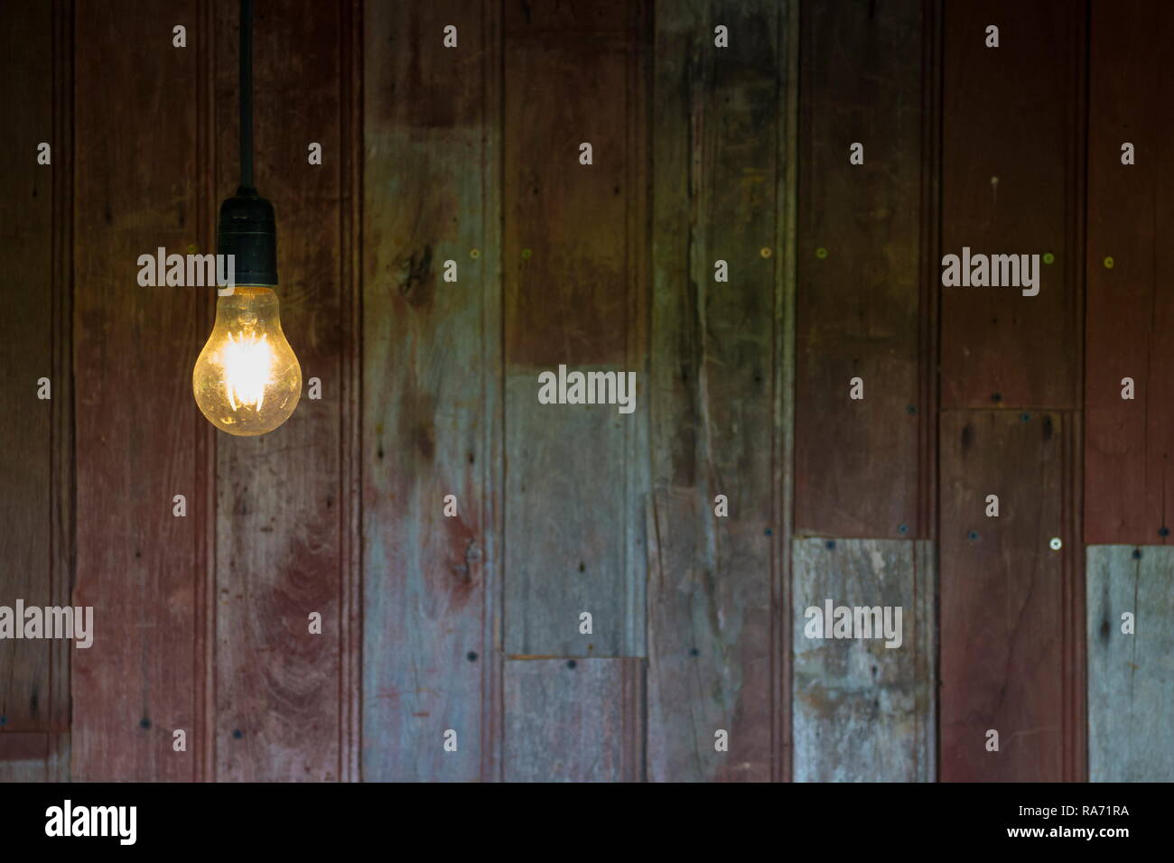 Light from vintage light bulb with old wood wall background, image with copy space. Stock Photo