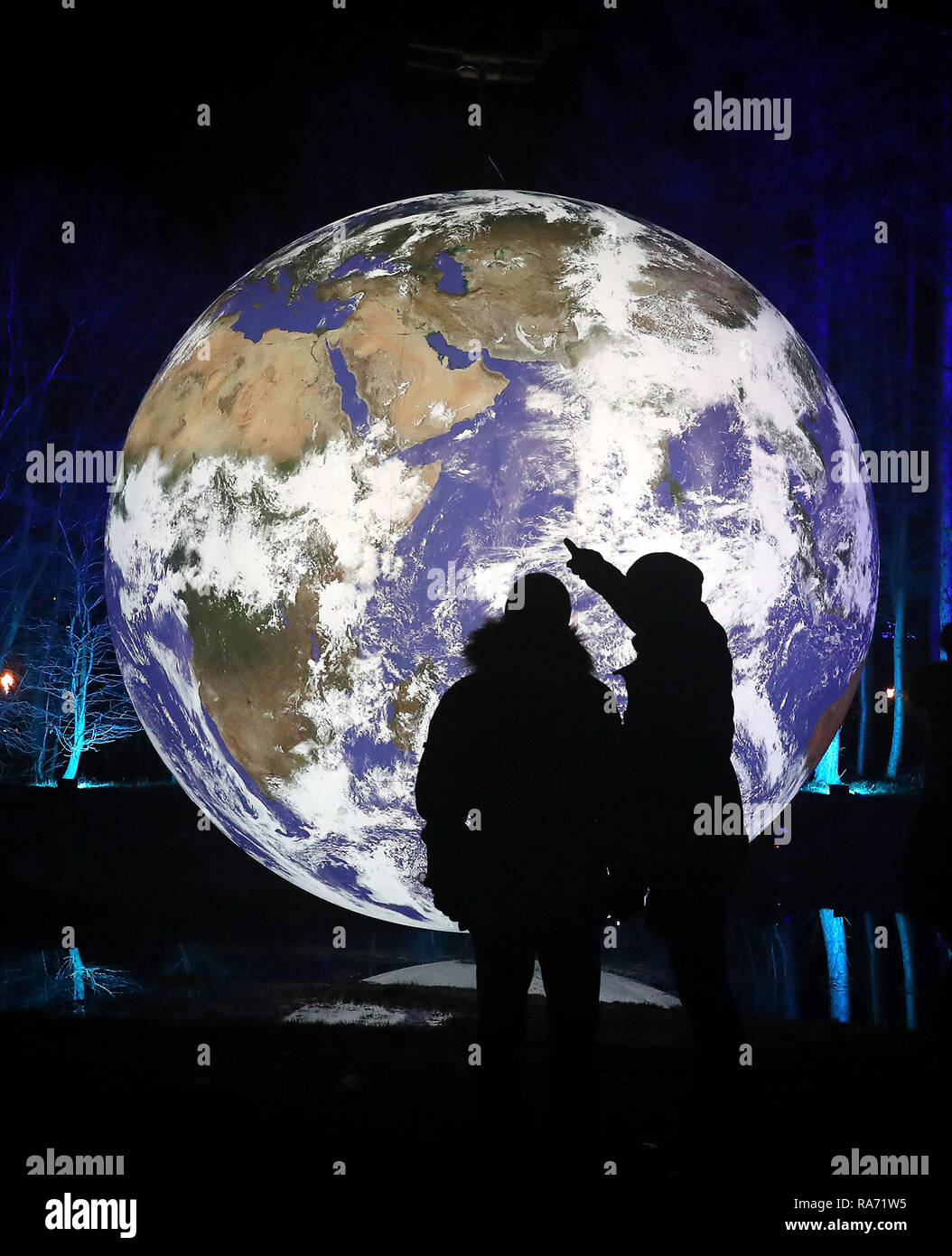 Visitors walks past the art installation Gaia, a seven-metre scale model of Earth created by artist Luke Jerram on the opening night of the Fire & Light: Cosmic Fortunes installation, an illuminated outdoor experience held at the Helix Park and the Kelpies in Falkirk. Stock Photo