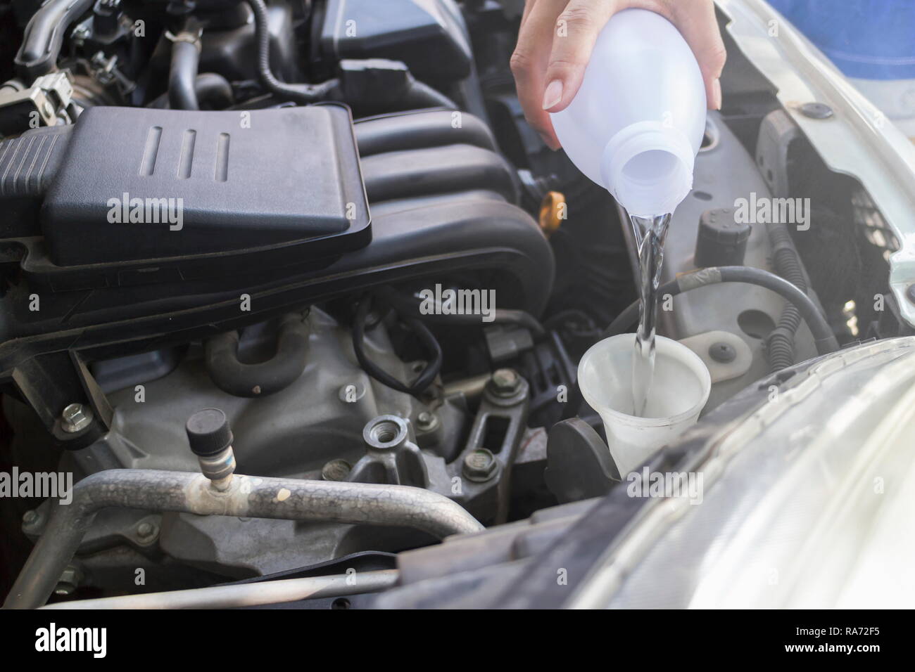 Mechanic filling water for windshield washer fluid to a car in the garage. Stock Photo