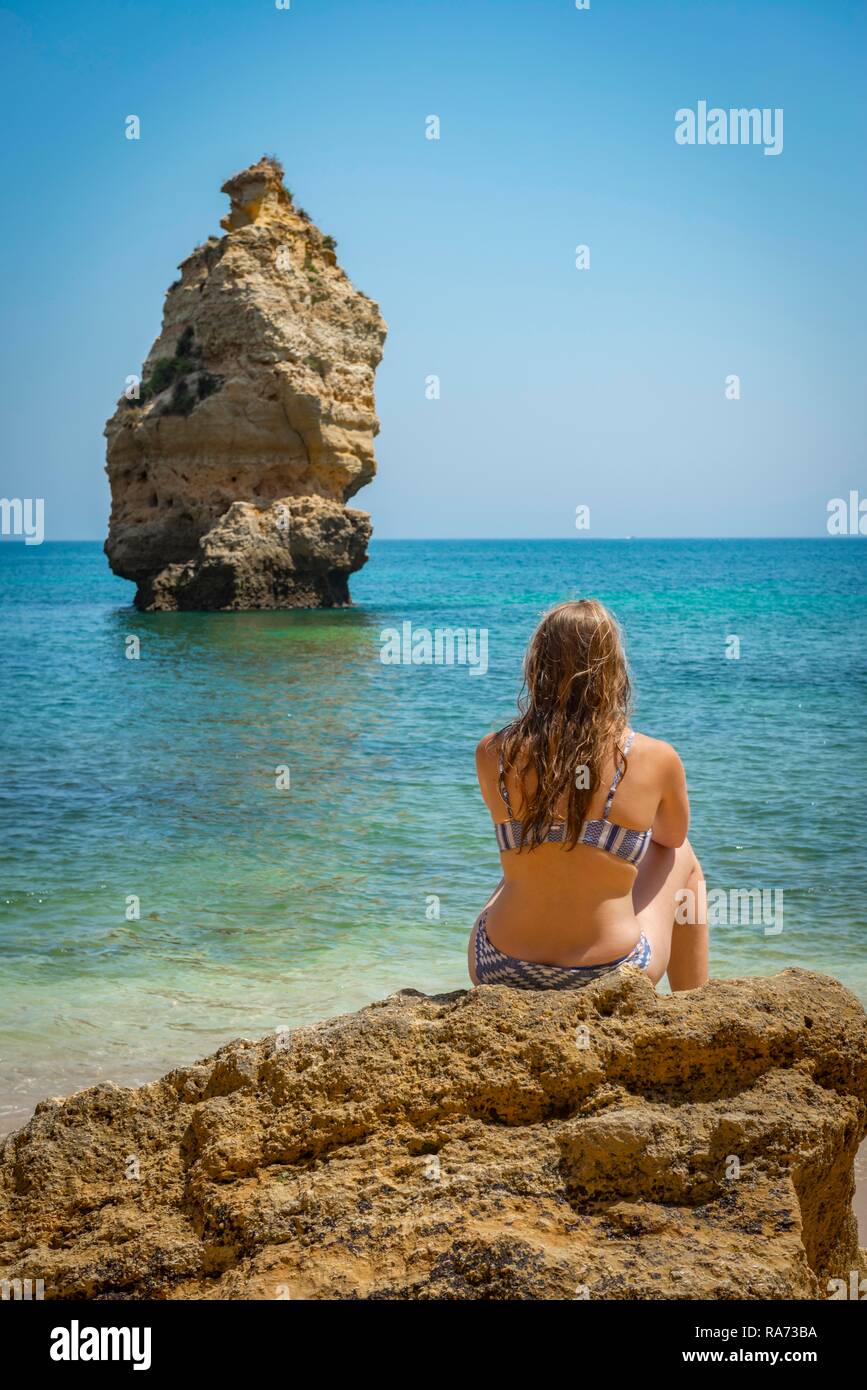 young-woman-sitting-on-a-rock-in-a-bikini-beach-praia-da-marinha
