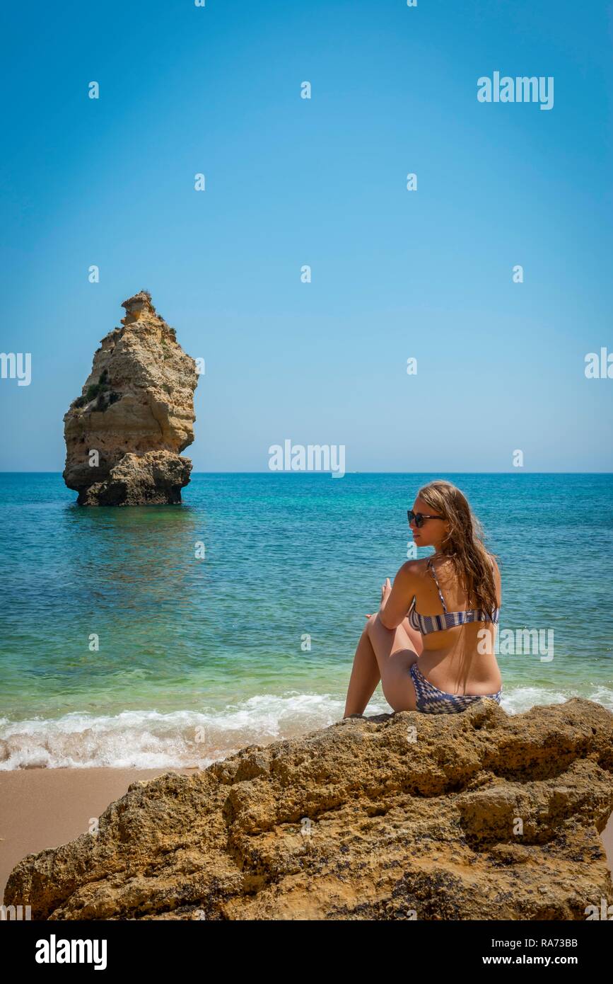 Young woman sitting on a rock in a bikini, beach Praia da Marinha, rocky  coast, rock formation in the sea, Algarve, Lagos Stock Photo - Alamy