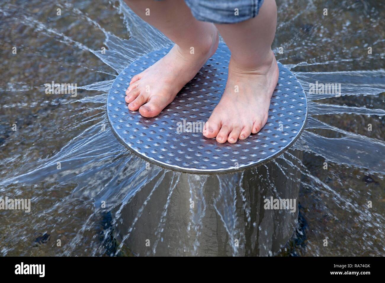 Child's feet on a metal plate with water squirting out Stock Photo