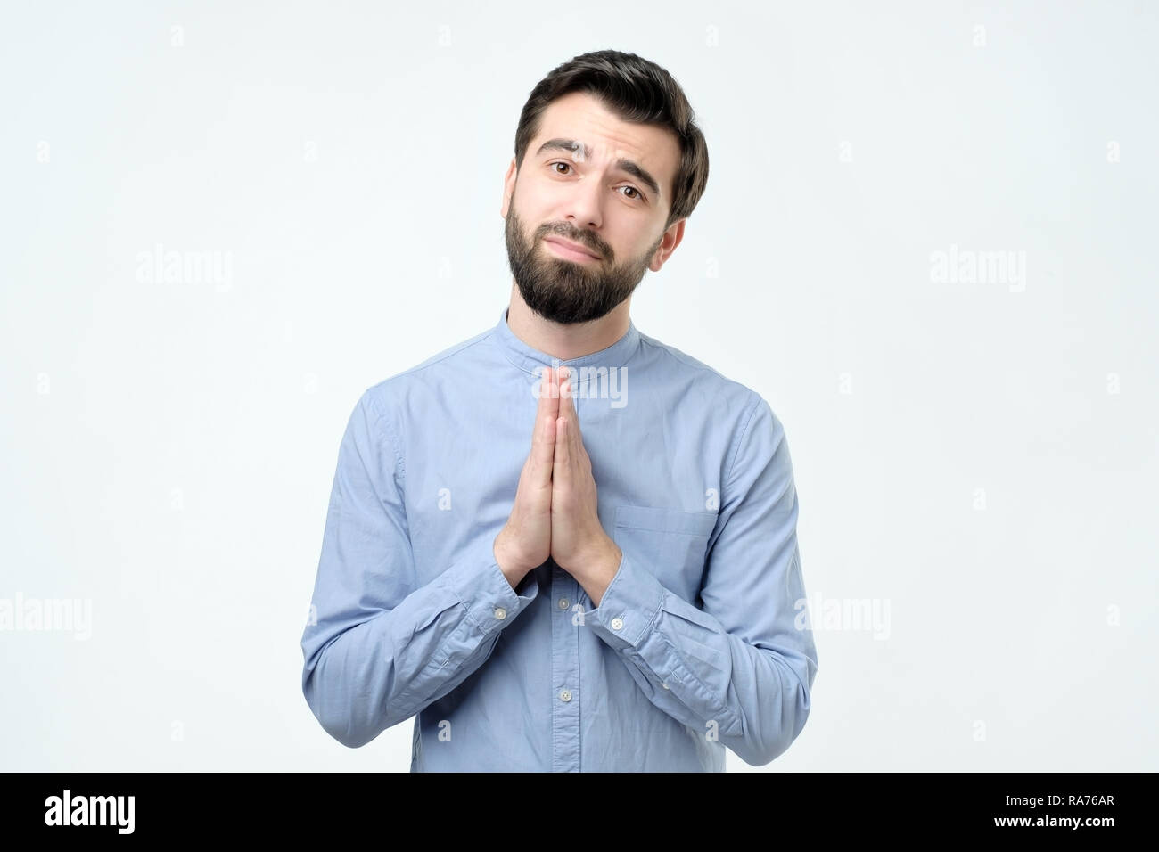 Guy in blue shirt holding hands in pray and gazing at camera hopefu Stock Photo
