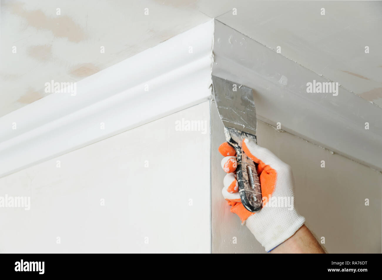 Installation of ceiling moldings. Worker puts glue on plastic molding