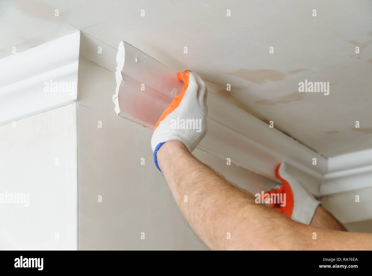 Installation of ceiling moldings. Worker fixes the plastic molding to the ceiling Stock Photo